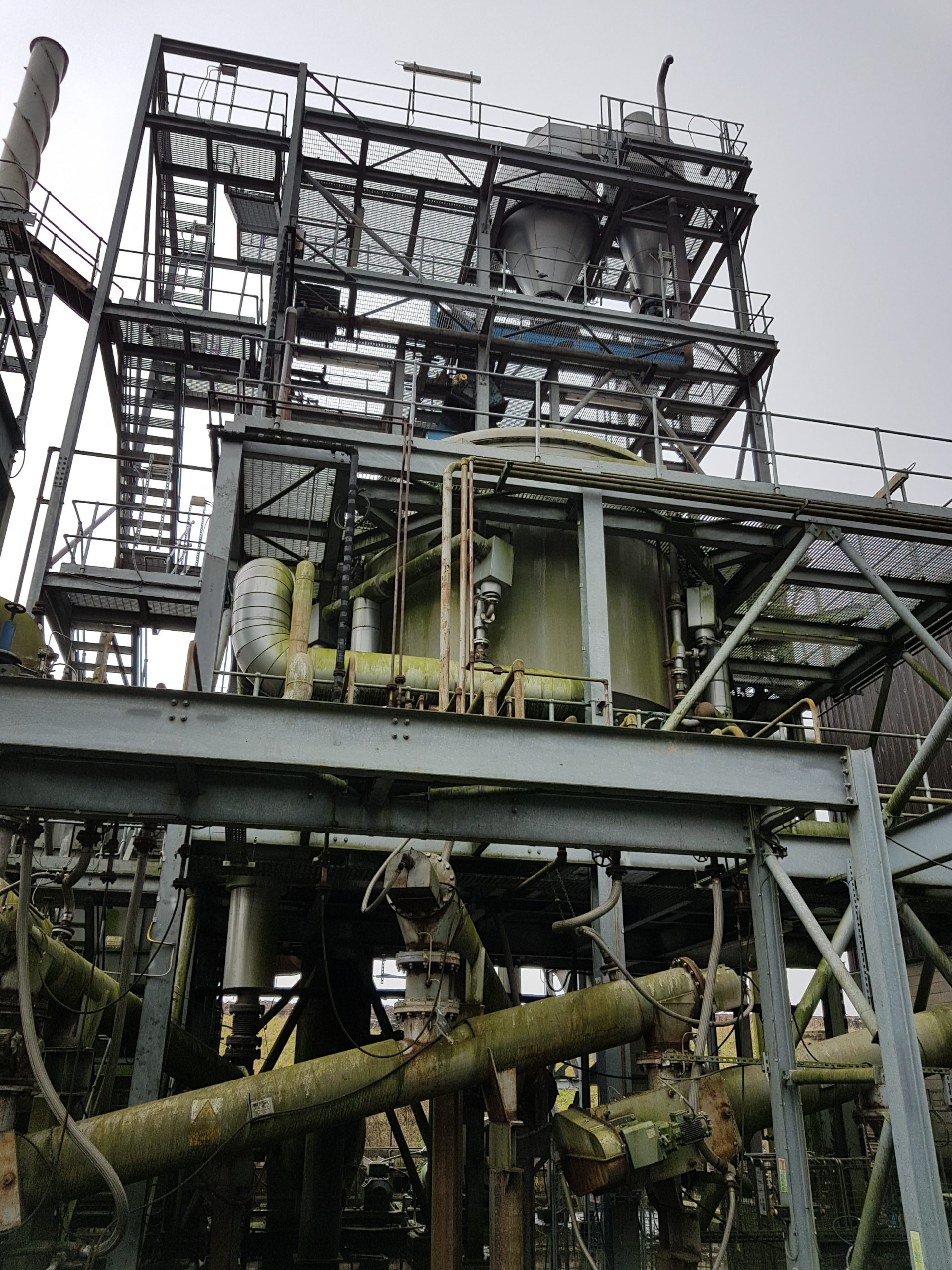 Images showing a dirty external process plant with vessels and inclined screw conveyors illustrating that later additions can restrict access for maintenance.